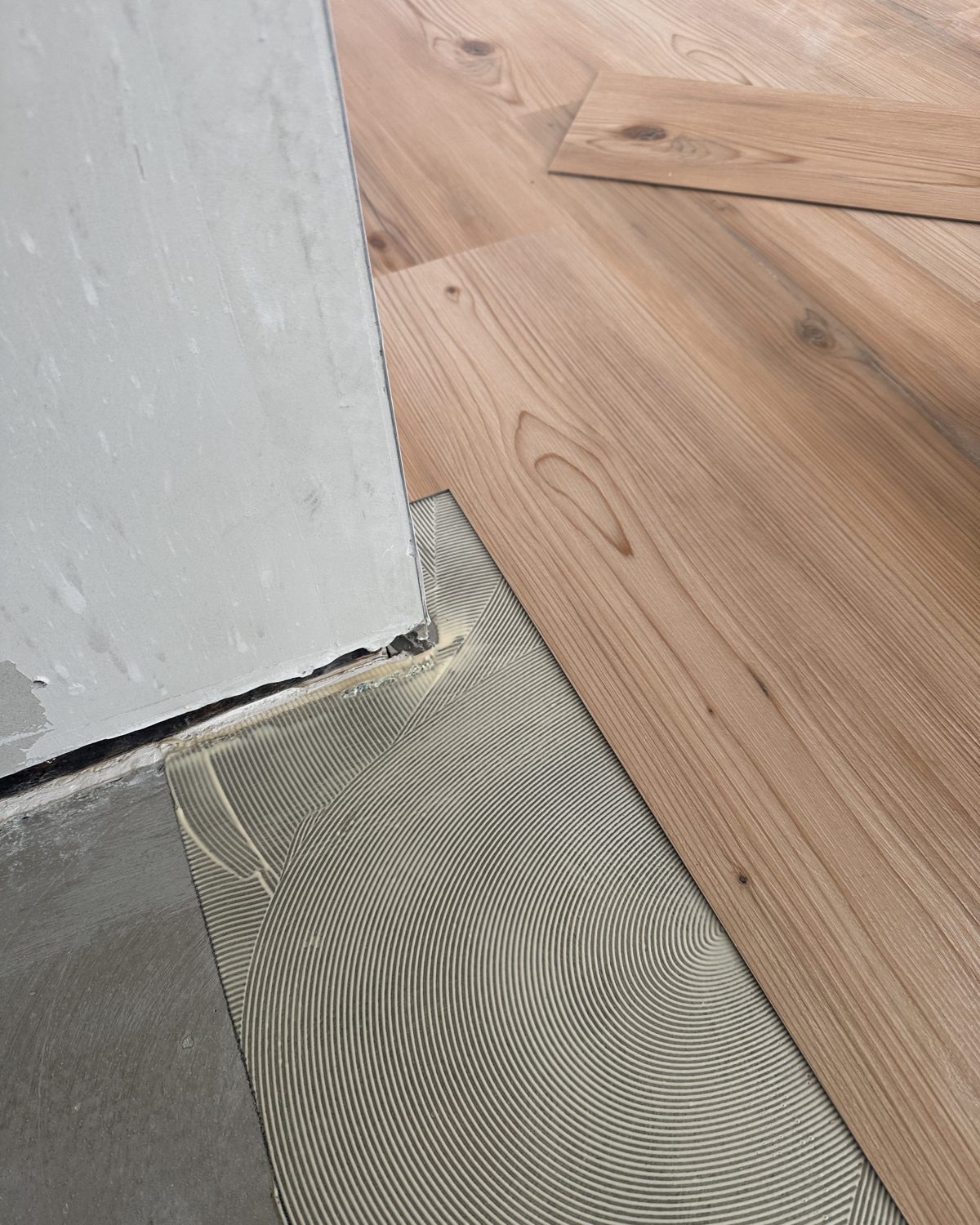 Gespachtelter Untergrund mit Kleberriefen neben bereits verlegten Vinylplanken