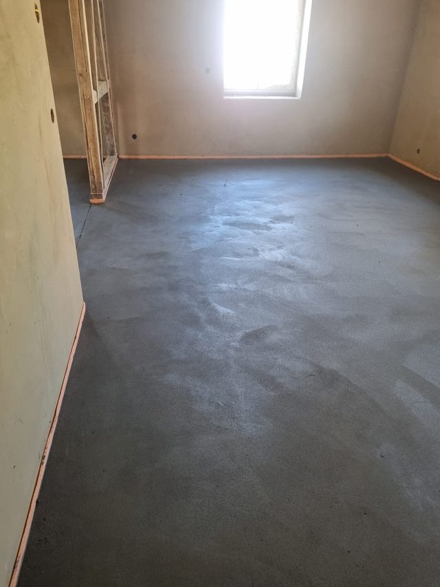Zementestrich, frisch abgezogen und matt, in einem Dachgeschossraum mit Holzständerwand