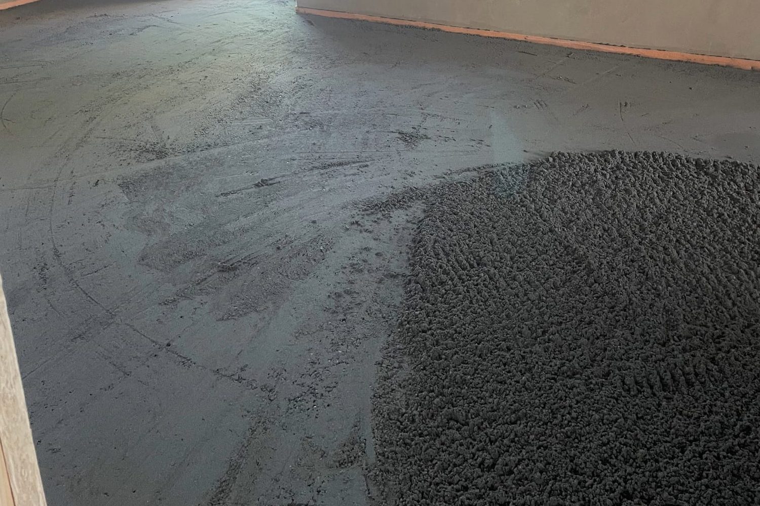 Zementestrich beim Einbau: ein Haufen erdfeuchter M&ouml;rtel auf der Fl&auml;che, daneben schon abgezogen; am Wandfu&szlig; der Randd&auml;mmstreifen