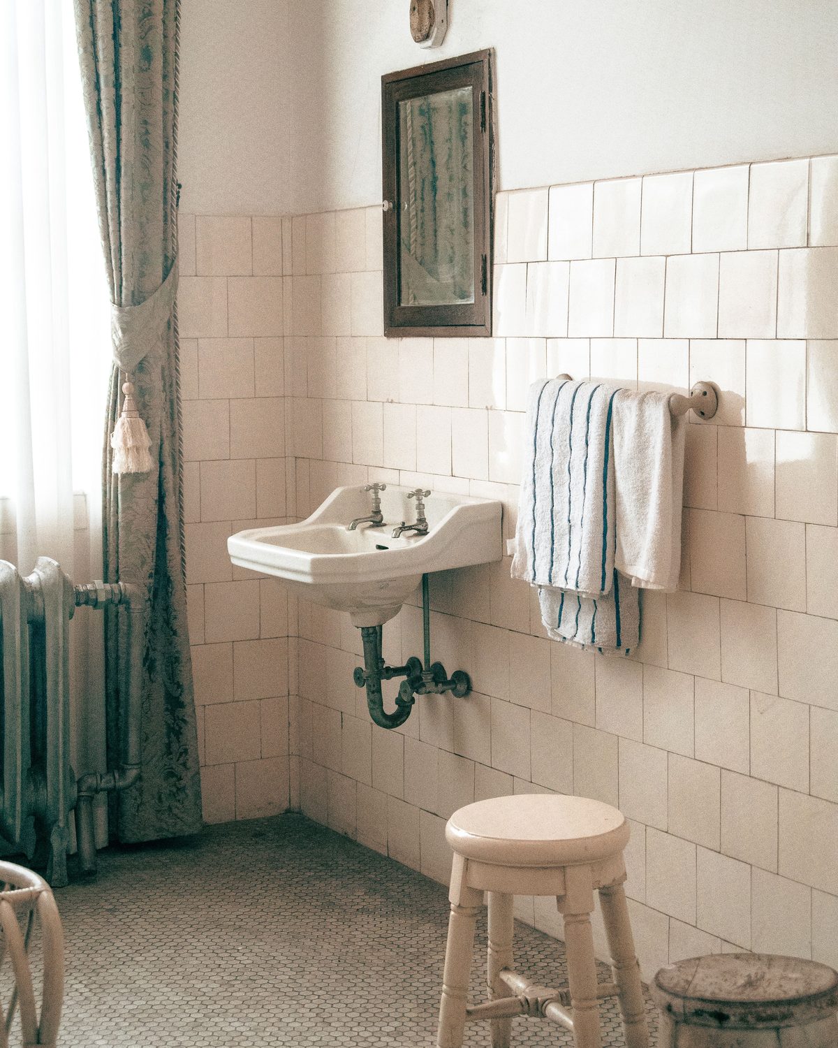 Altes Bad mit kleinen Wandfliesen, Waschbecken an der Wand, Heizk&ouml;rper und Hocker