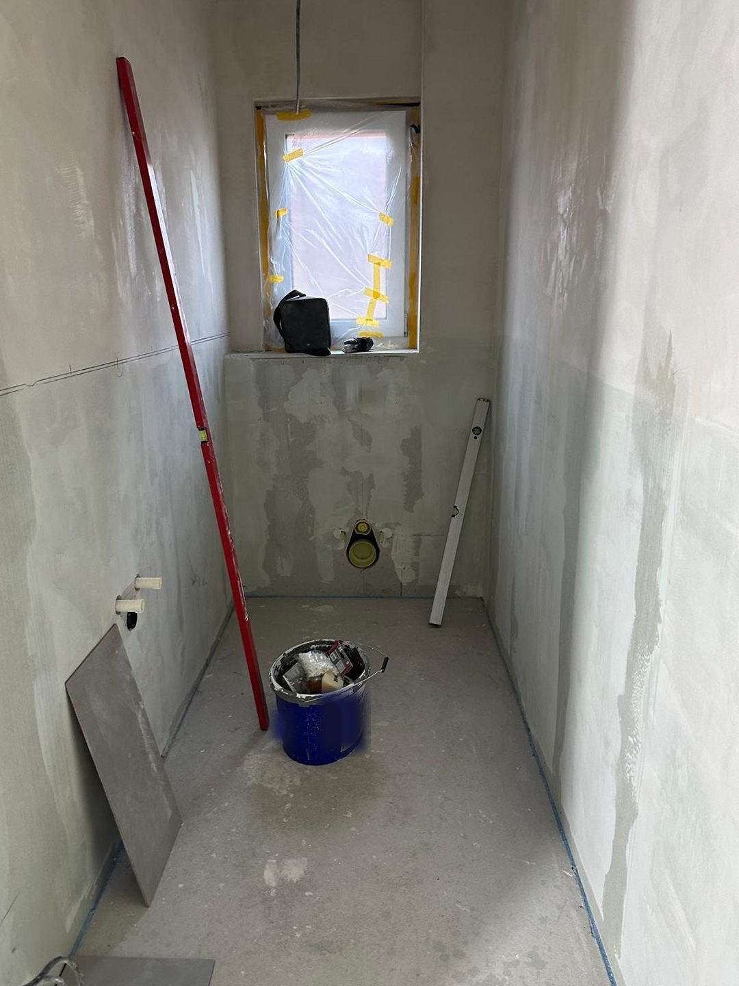 G&auml;ste-WC im Rohbau: verputzte W&auml;nde, abgeklebtes Fenster, Vorwandelement, Leiter und Eimer