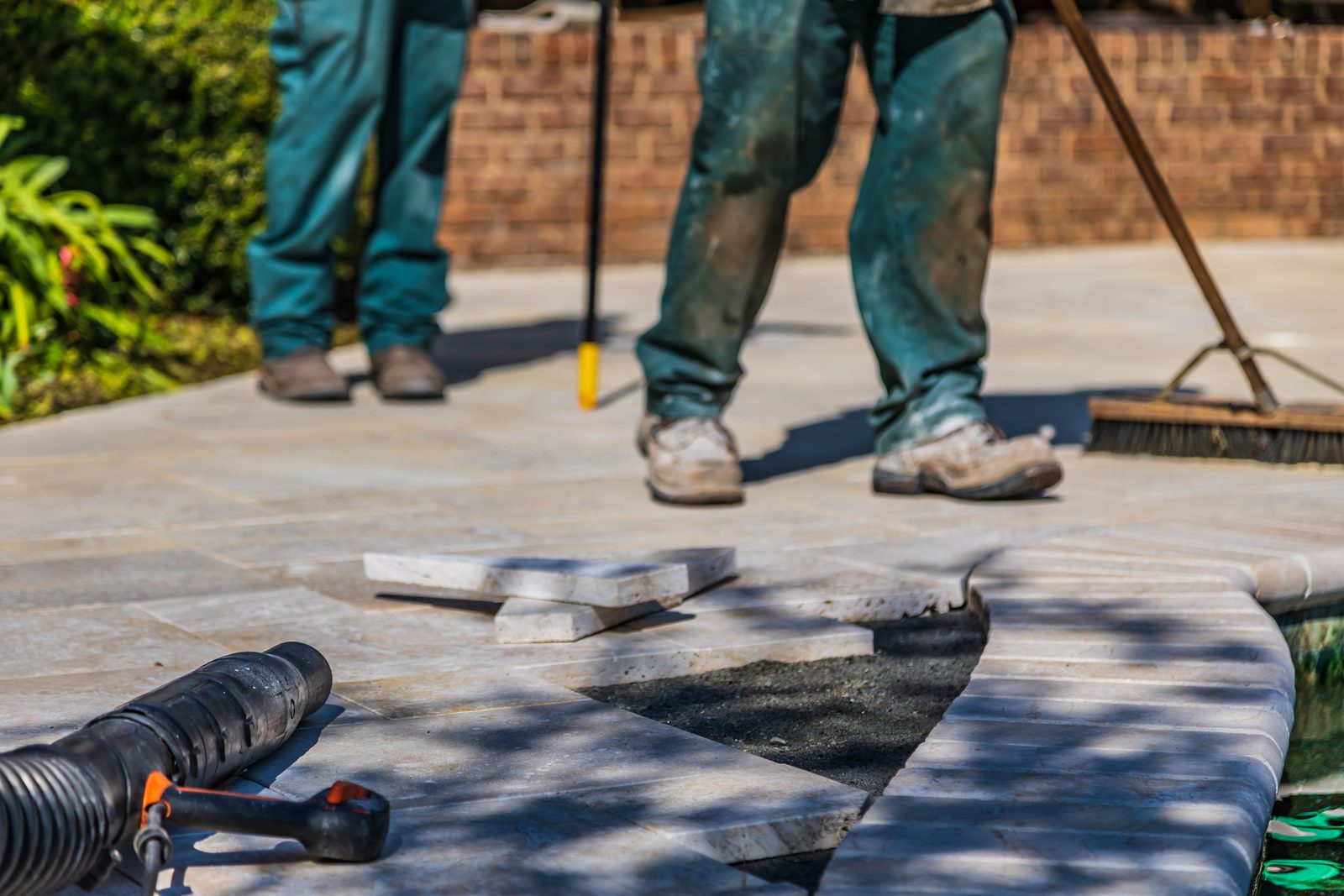 Terrassenplatten werden im Freien verlegt, im Hintergrund die Beine zweier Handwerker