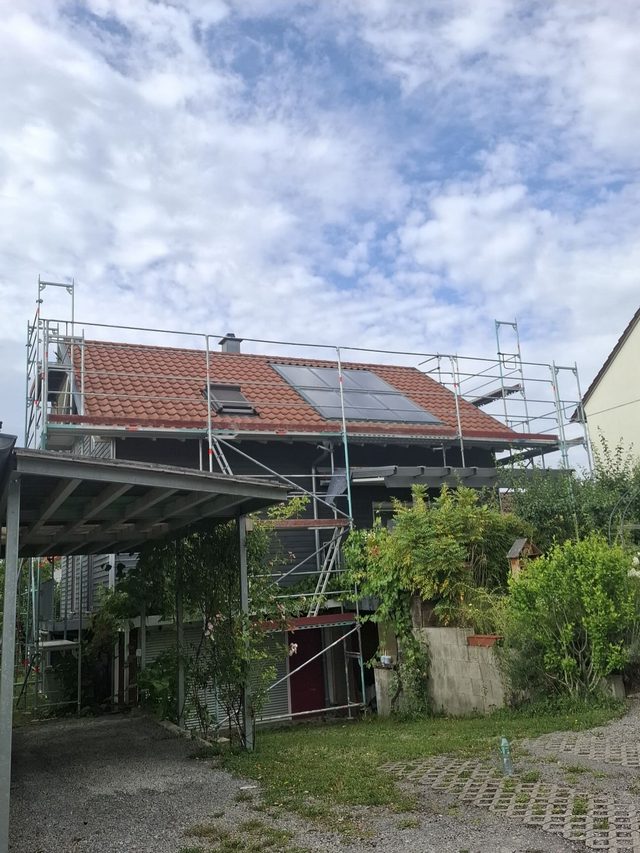 Haus mit Ziegeldach und Solaranlage, Ger&uuml;st bis zur Traufe, davor ein Carport und Garten