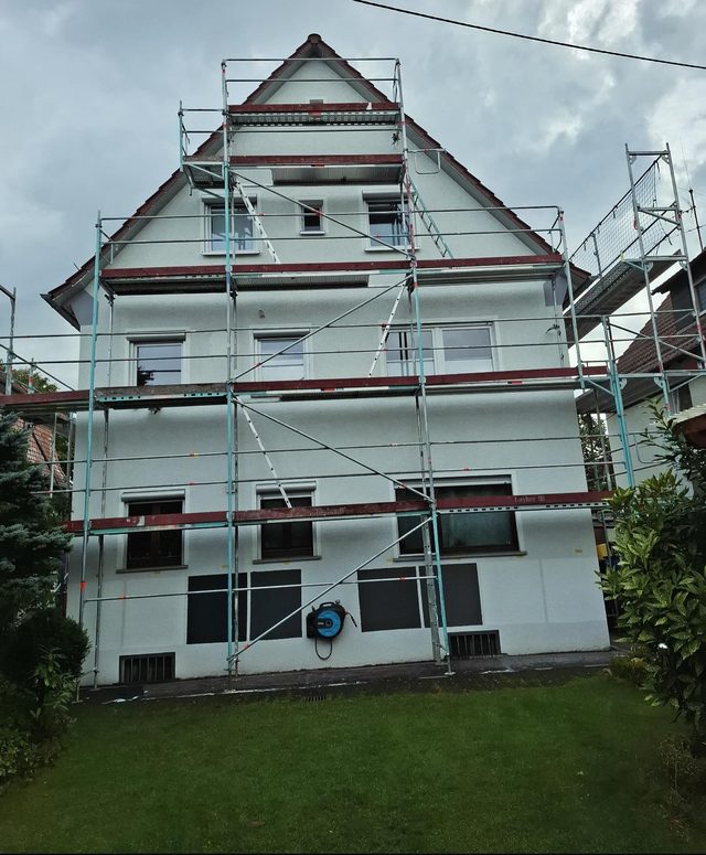 Wei&szlig;e Giebelwand eines Einfamilienhauses mit Ger&uuml;st &uuml;ber alle Geschosse bis zur Giebelspitze, davor Rasen