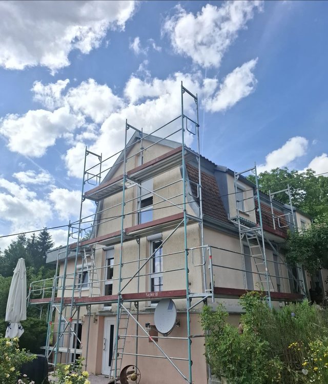 Einfamilienhaus mit Gauben, an Giebel und L&auml;ngsseite einger&uuml;stet, blauer Himmel mit Wolken
