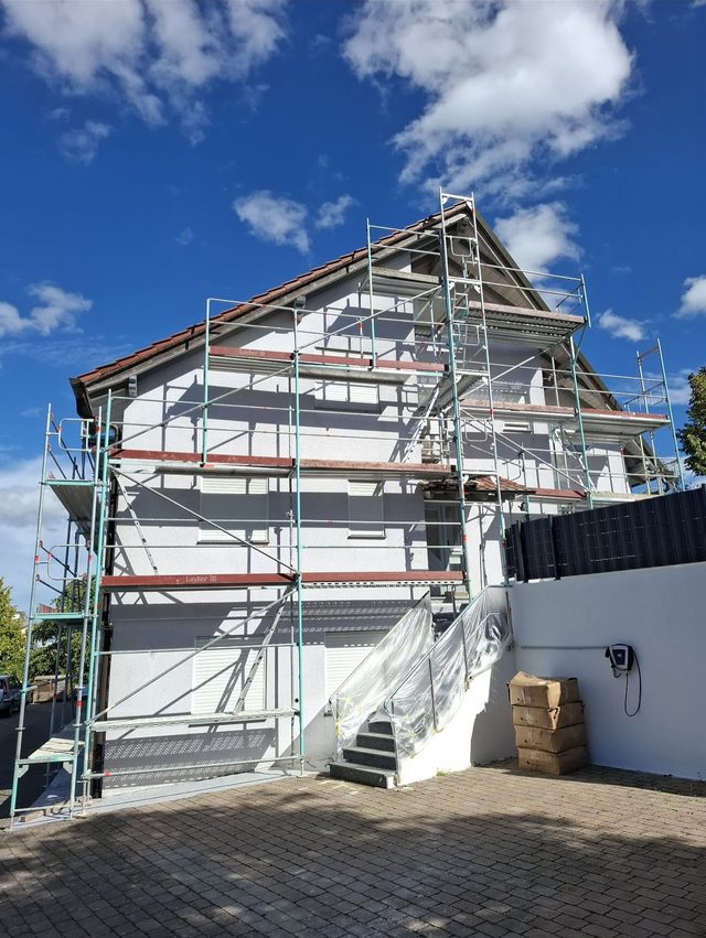 Frisch verputztes Haus mit Ger&uuml;st &uuml;ber drei Lagen, die Au&szlig;entreppe mit Folie gesch&uuml;tzt, gepflasterter Hof