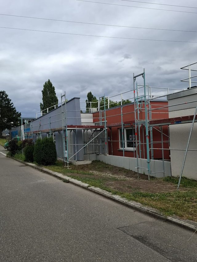 Flachbau an einer Stra&szlig;e, Ger&uuml;st an der Fassade mit Gel&auml;nder &uuml;ber dem Dachrand