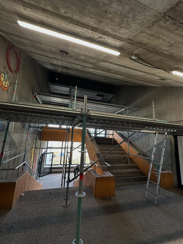 Ger&uuml;st unter einer Betondecke in einem hohen Raum, darunter eine Treppe und eine Leiter