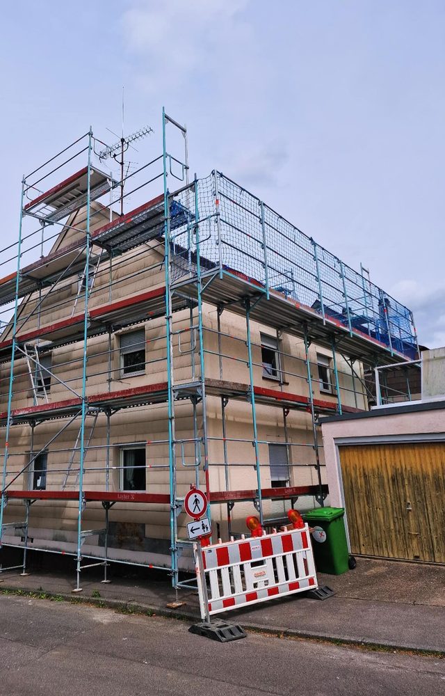 Einger&uuml;stetes Wohnhaus an einer Stra&szlig;e, davor rot-wei&szlig;e Absperrung mit Warnleuchten und Schild f&uuml;r Fu&szlig;g&auml;nger