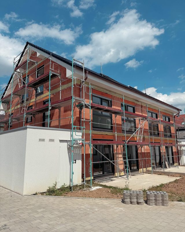 Rohbau aus Ziegeln mit eingesetzten Fenstern, Ger&uuml;st &uuml;ber die ganze Fassade, davor Pflaster