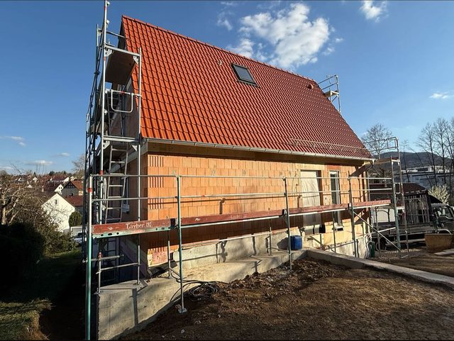 Neubau mit neuem rotem Ziegeldach, Ger&uuml;st an der Fassade, im Hintergrund H&auml;user