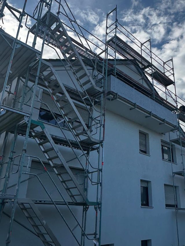 Ger&uuml;st mit Treppenaufg&auml;ngen an einem wei&szlig;en Mehrfamilienhaus, Himmel mit Wolken