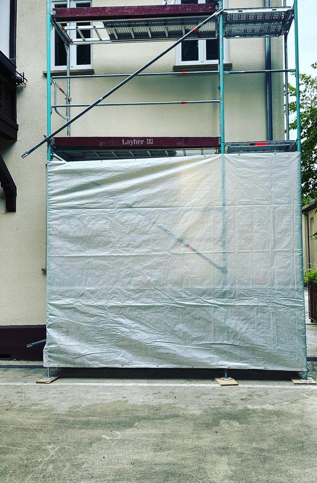 Ger&uuml;st vor einer Hauswand, die untere Lage mit einer wei&szlig;en Plane verkleidet