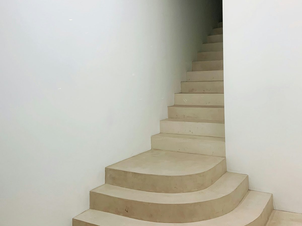 Betontreppe ohne Belag mit gerundeten unteren Stufen in einem wei&szlig; verputzten Raum