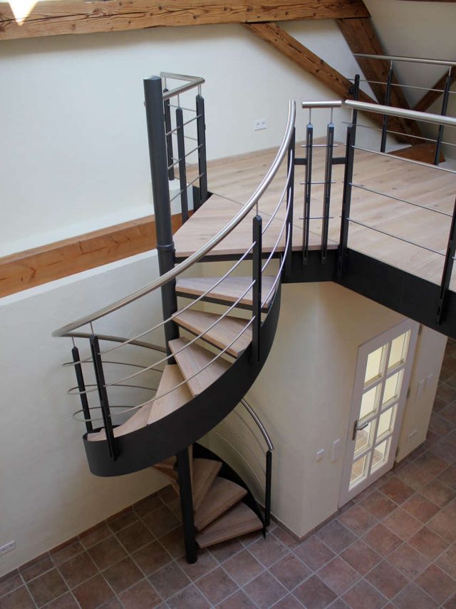 Spindeltreppe aus Stahl mit Holzstufen und gebogenem Edelstahlgeländer, von oben gesehen
