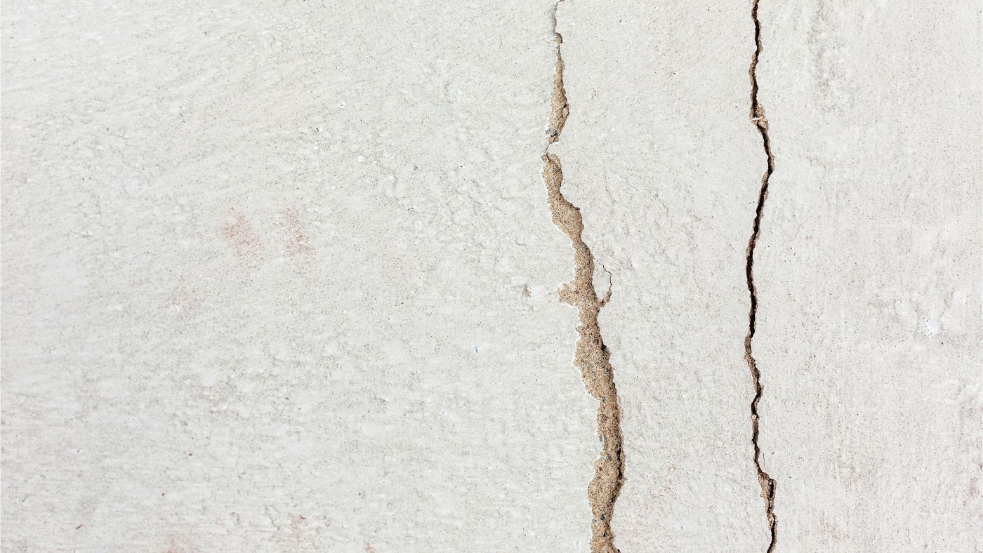 Zwei feine Risse laufen senkrecht durch eine hell gestrichene Wand