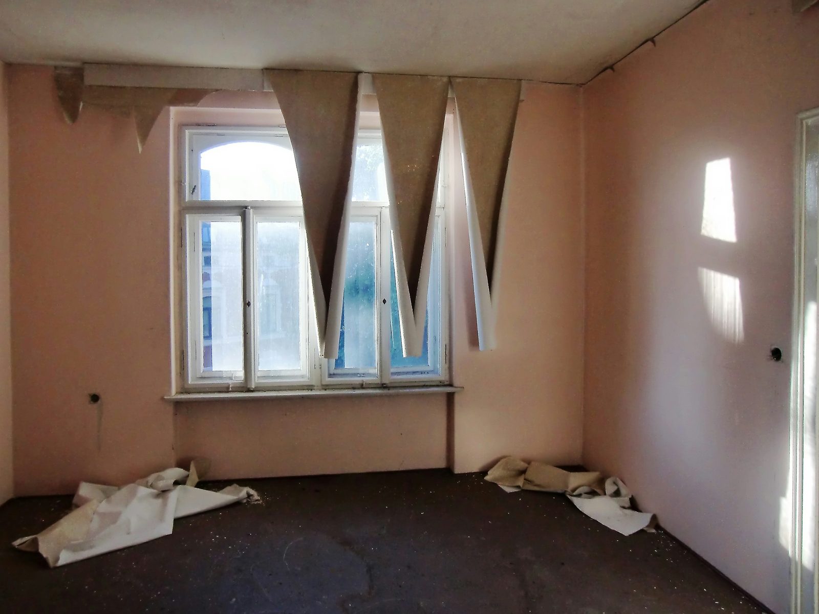 Leerer Altbauraum, von der Decke hängen Bahnen alter Tapete herab, am Boden liegen abgelöste Reste