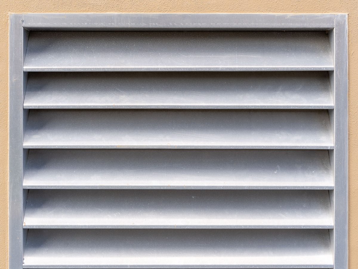 Graues L&uuml;ftungsgitter mit Lamellen in einer beige verputzten Au&szlig;enwand