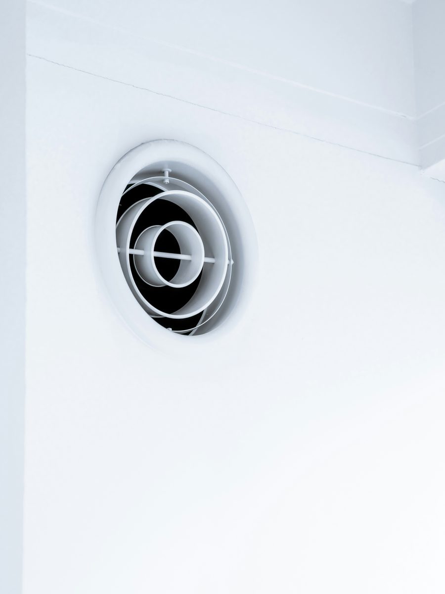 Rundes weißes Luftventil in einer weißen Wand nahe der Decke